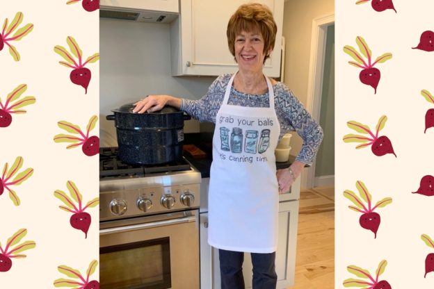 A smiling woman wearing an apron next to a canning pot.